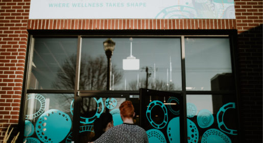 Front door of Foundry Kelowna two people hugging and facing the front of foundry kelowna, brick walls surround the glass doors of the building