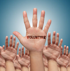 Hands raised with the text VOLUNTEER written on the palms