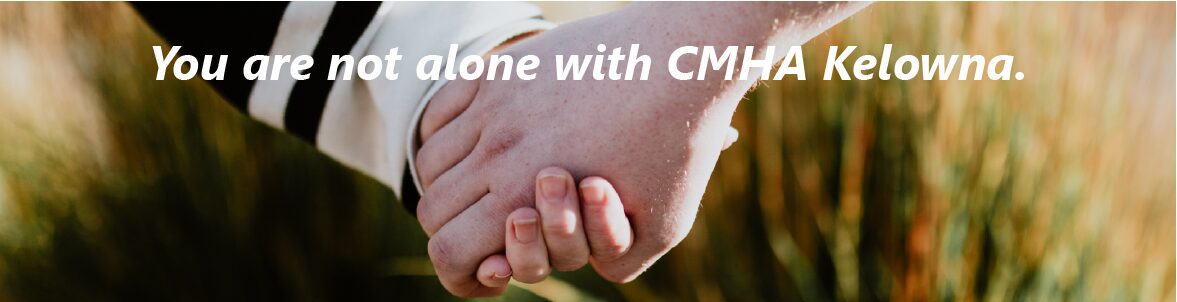 holding hands in a field with the text "you are not alone with CMHA Kelowna" stretching across