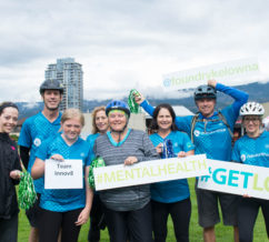 Eight people with bicycle helmets and CMHA Blue shirts holding signs for # Get Loud fundraisers
