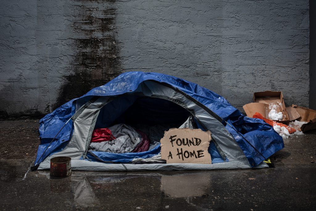 a tent sitting open on a street where someone who was previously homeless used to live. the open fly of the tent reveals a carboard sign that reads "found a home"