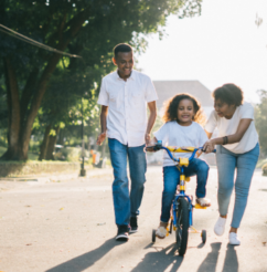 A family growing their lives by teaching their child to ride a bike with training wheels on