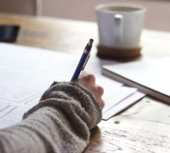 writing with pen and a paper on a desk with coffee, writing down their wellness recovery action plan? Maybe!