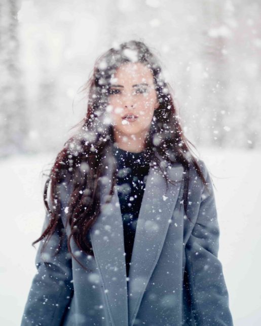 SAD CMHA woman with long hair and a winter coat standing outside as it snows heavily