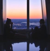 a parent and their child siting in front of a wide window wile the sun sets talking about mental health