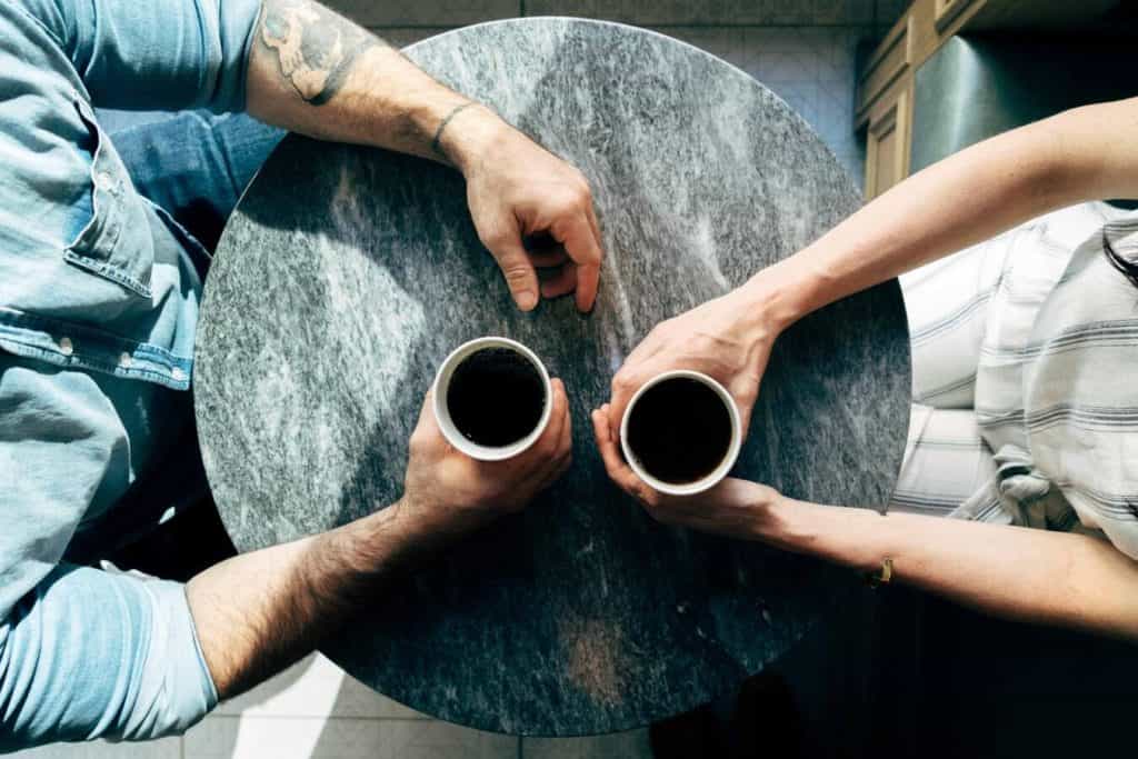2 people sit at a stable having coffee and discussing their mental health